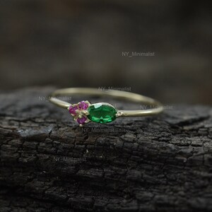 May include: A delicate gold ring with a green gemstone and pink accent stones. The ring is on a dark wood surface.