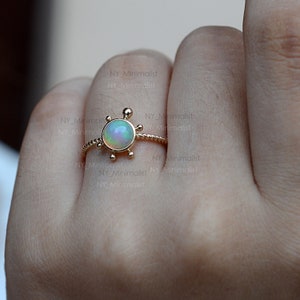 May include: A gold ring with a delicate rope design and a small opal gemstone set in a compass-shaped bezel. The ring is on a finger.