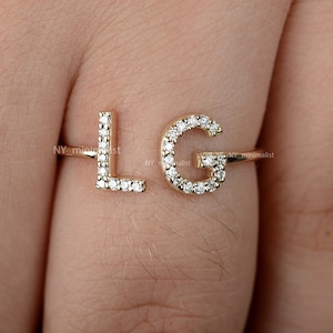 Puede incluir: Anillo de oro con dos letras, L y G, engastadas con pequeños diamantes. El anillo está en un dedo.