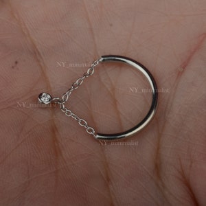May include: A silver ring with a small diamond on a chain attached to the ring.
