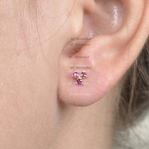 Pode incluir: Close-up de uma orelha com um pequeno brinco de ouro com três pedras preciosas cor-de-rosa em forma de trevo.