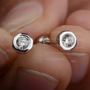 Puede incluir: Un par de pendientes de plata con un diamante redondo y transparente en cada uno. Los diamantes están engastados en una forma hexagonal.