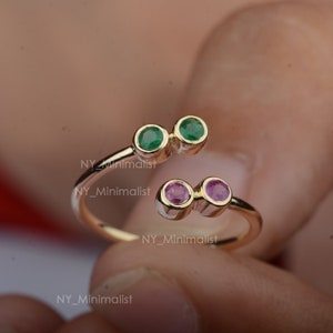 May include: Gold ring with two green gemstones and two pink gemstones. The ring is open and has a simple design.