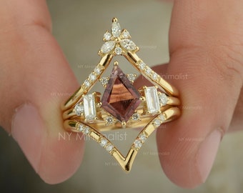 Puede incluir: Un juego de tres anillos de oro con una gran piedra preciosa facetada de color marrón rojizo rodeada de diamantes más pequeños. El anillo central presenta un diseño geométrico con una parte superior puntiaguda.