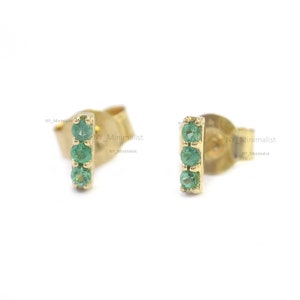 May include: A pair of gold earrings with three emerald green gemstones set in a vertical line.