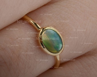 Può includere: Un anello d'oro con una pietra di opale verde. L'anello è semplice ed elegante, con una fascia sottile e una montatura a castone per l'opale.