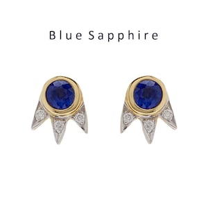 May include: A pair of gold and silver earrings with a blue sapphire gemstone in the center of each earring. The earrings have a starburst design with small diamonds around the sapphire.