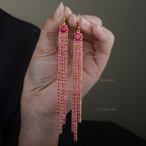 May include: Gold-coloured drop earrings with a cascade of small, pink gemstones. Each earring has a large, oval-shaped, red gemstone at the top. The earrings are held up by a gold hook.