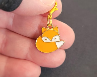 May include: A gold-coloured charm featuring a sleeping orange fox with a white tail tip. The charm has a lobster clasp.