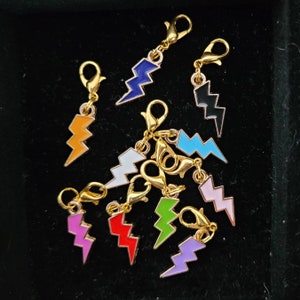 May include: A set of ten colourful lightning bolt charms with gold clasps. The charms are made of metal and have a glossy enamel finish. The colours include blue, orange, white, black, light blue, pink, red, green, and purple.