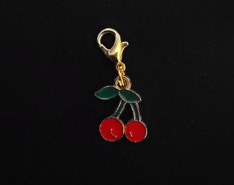 May include: A gold charm featuring a red cherry design. The charm has a green stem and leaves and a gold lobster clasp.