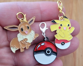 May include: Three gold-tone charms featuring Pokemon characters. The first charm is a brown Eevee with a gold-tone clasp. The second charm is a yellow Pikachu with a red and white Pokeball. The third charm is a red and white Pokeball with a gold-tone clasp.