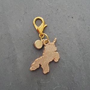 May include: Gold-toned charm featuring a unicorn silhouette with a small round bead attached to a gold-toned lobster clasp.