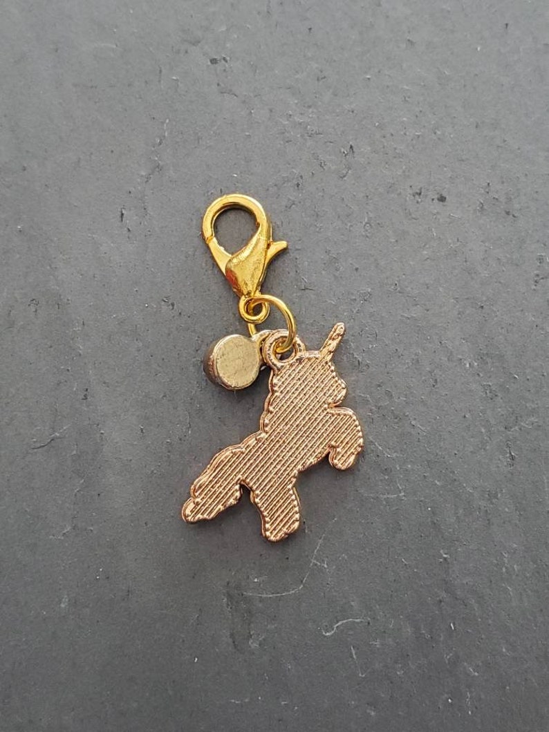 May include: Gold-toned charm featuring a unicorn silhouette with a small round bead attached to a gold-toned lobster clasp.