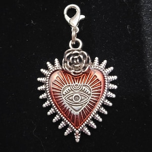 May include: Silver charm with a red heart with a silver eye design and a silver rose on top. The heart has a silver border with spikes.