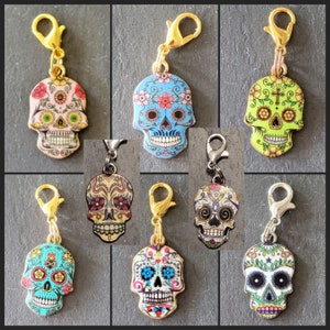 May include: Ten colorful sugar skull charms with gold metal loops. Each charm features a different design with flowers, cross, and other details.