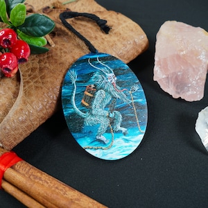 Op de afbeelding: Een ronde houten ornament met een blauwe achtergrond en een wit, harig wezen met een lange tong en een vat op zijn rug. Het wezen is vastgeketend en lijkt door een besneeuwd landschap te rennen.