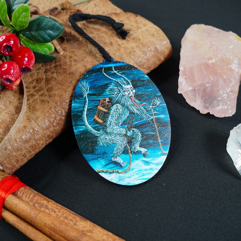 Op de afbeelding: Een ronde houten ornament met een blauwe achtergrond en een wit, harig wezen met een lange tong en een vat op zijn rug. Het wezen is vastgeketend en lijkt door een besneeuwd landschap te rennen.