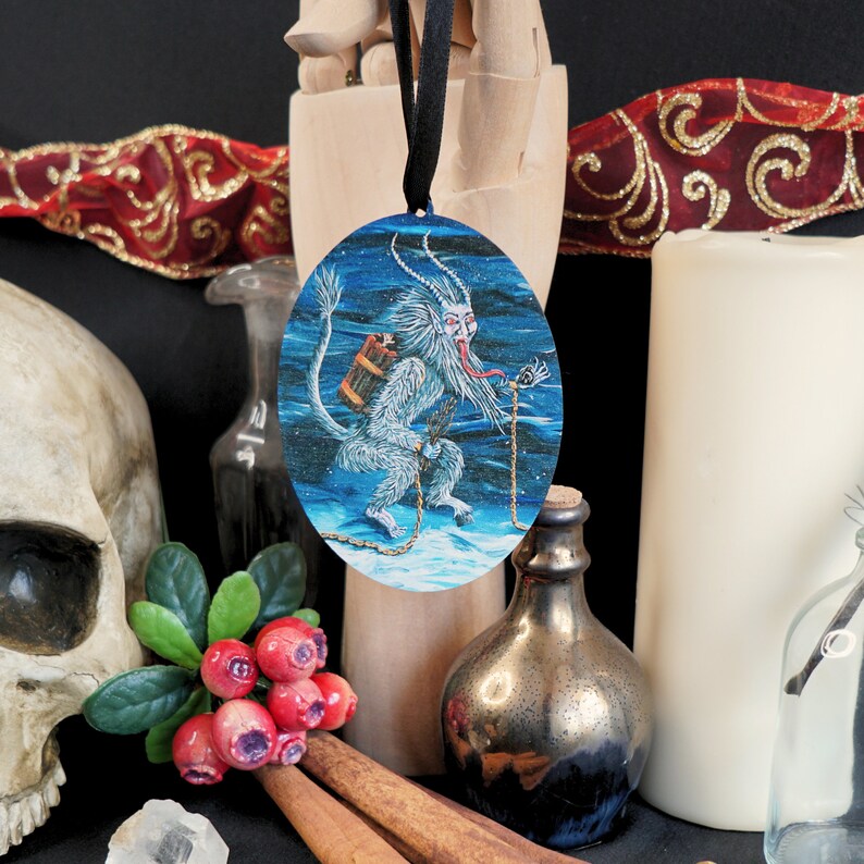 Op de afbeelding: Een ronde, blauw-witte kerstbal met een wit, harig wezen met een lange, rode tong en een vat op zijn rug. Het wezen staat op een besneeuwde ondergrond met een ketting.