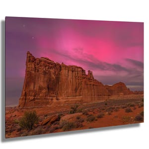 May include: A landscape print featuring a towering red rock formation under a vibrant pink and purple sky. The desert scene includes sparse vegetation and a hint of stars, creating a dramatic and colorful display.