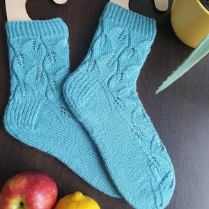 Könnte beinhalten: Ein Paar tealblaue Stricksocken mit einem zarten Blattmuster. Die Socken sind aus weichem Garn gefertigt und haben eine bequeme Passform.