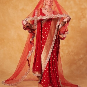 May include: A vibrant red sari with gold accents and intricate detailing. The sari features a matching red veil with delicate gold trim. The ensemble includes gold jewelry, creating a festive and elegant look.
