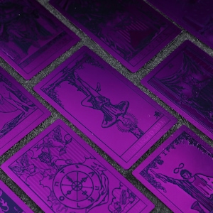 Pu&ograve; includere: Un set di carte dei tarocchi con lamina metallica viola e inchiostro blu. Le carte presentano varie immagini dai Tarocchi Maggiori, tra cui L'Impiccato, La Ruota della Fortuna e Il Carro.