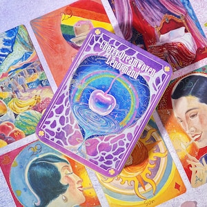 May include: A collection of colorful tarot cards featuring illustrations. One card displays the text "Cherry Dreamwoven Lenormand" with a cherry and rainbow design. Other cards depict scenes of a market, a bed, a man, and the sun.