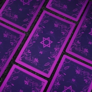 Pu&ograve; includere: Un set di carte dei tarocchi con un design viola e nero. Le carte presentano una stella di David e motivi floreali.