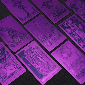 Pu&ograve; includere: Un set di nove carte dei tarocchi con sfondi metallici viola e illustrazioni in bianco e nero. Le carte sono disposte a ventaglio su una superficie grigio scuro.