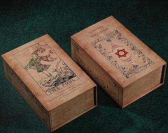 May include: Two brown cardboard boxes with a vintage design. The box on the left features a tarot card illustration of "The Fool" with a person standing on a cliff. The box on the right has the text "The Neo Rider Tarot Collection".