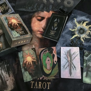 May include: A tarot card set including a box, guidebook, and a drawstring bag. The box and bag feature a sun design. Individual cards display illustrations and the text "THE RUINED BRIDGES TAROT". The set is arranged on a dark surface.