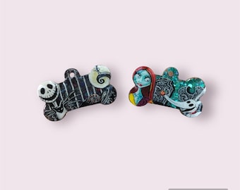 May include: Two bone-shaped dog tags with images of characters from the Nightmare Before Christmas. One tag features Jack Skellington with a black and white background, and the other tag features Sally with a green and blue background.