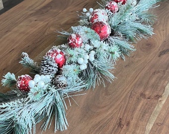 Pièce maîtresse de Noël, décor de table longue, boules rouges, baies blanches givrées, cônes d’aiguilles de pin enneigés, décor de cheminée de table basse