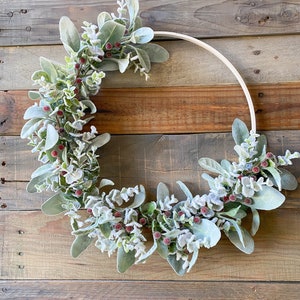 May include: A frosted eucalyptus and berry wreath on a wooden background. The wreath is made of faux eucalyptus leaves and berries, and is decorated with a white frost.
