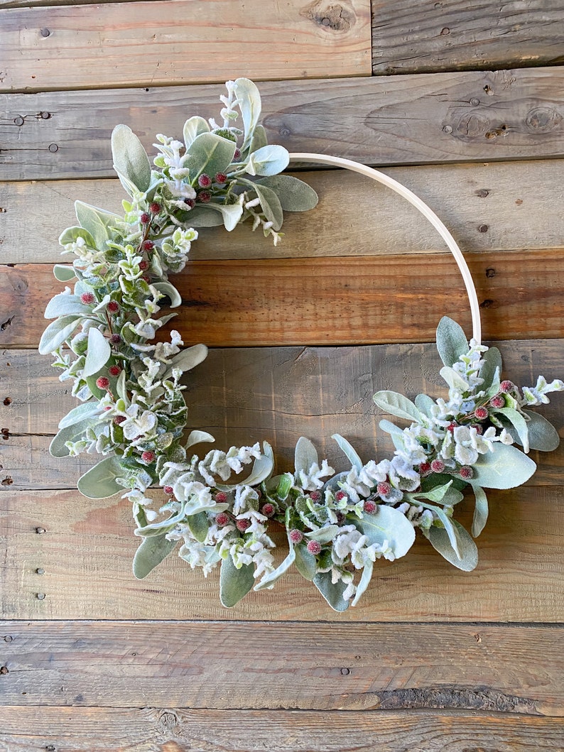 May include: A frosted eucalyptus and berry wreath on a wooden background. The wreath is made of faux eucalyptus leaves and berries, and is decorated with a white frost.