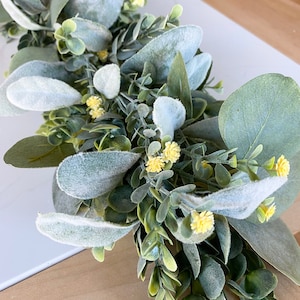 Puede incluir: Una guirnalda artificial de eucalipto verde y gris con peque&ntilde;as flores amarillas. La guirnalda est&aacute; hecha de hojas y flores falsas y es perfecta para agregar un toque de vegetaci&oacute;n a la decoraci&oacute;n de tu hogar.