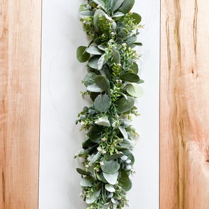 Puede incluir: Una larga guirnalda de vegetaci&oacute;n artificial con peque&ntilde;as hojas verde claro y bayas blancas. La guirnalda es perfecta para a&ntilde;adir un toque de naturaleza a la decoraci&oacute;n de tu hogar.