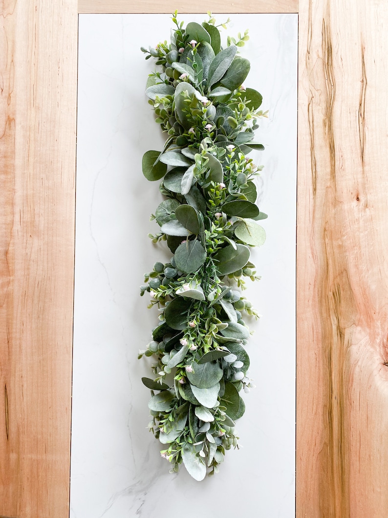 Puede incluir: Una larga guirnalda de vegetaci&oacute;n artificial con peque&ntilde;as hojas verde claro y bayas blancas. La guirnalda es perfecta para a&ntilde;adir un toque de naturaleza a la decoraci&oacute;n de tu hogar.