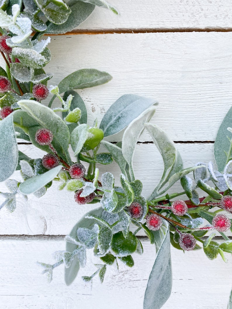 May include: A frosted eucalyptus wreath with red berries. The wreath is made of artificial greenery and is perfect for adding a touch of winter to your home decor.