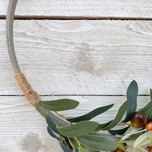 May include: A rustic wooden wreath with a brown twine accent and a green olive branch with brown olives.