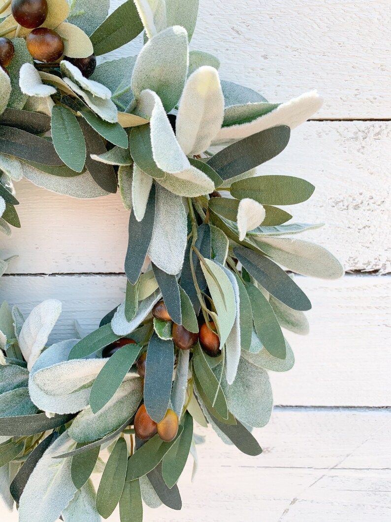 May include: A green and gray olive branch wreath with brown olives. The wreath is made of artificial leaves and is perfect for decorating a home or office.