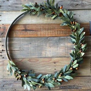 May include: A green olive branch wreath with brown berries, hanging on a rustic wooden wall.
