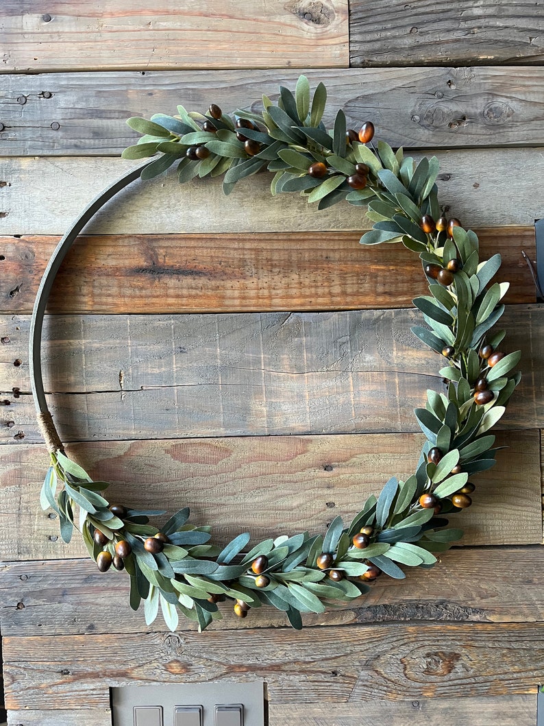 May include: A green olive branch wreath with brown berries, hanging on a rustic wooden wall.