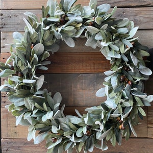 May include: A green and gray faux lamb's ear wreath with brown berries.