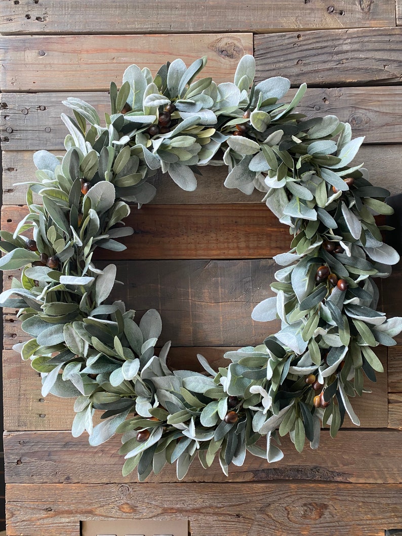 May include: A green and gray faux lamb's ear wreath with brown berries.