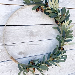 May include: A green olive branch wreath with brown olives, wrapped around a natural wood hoop.