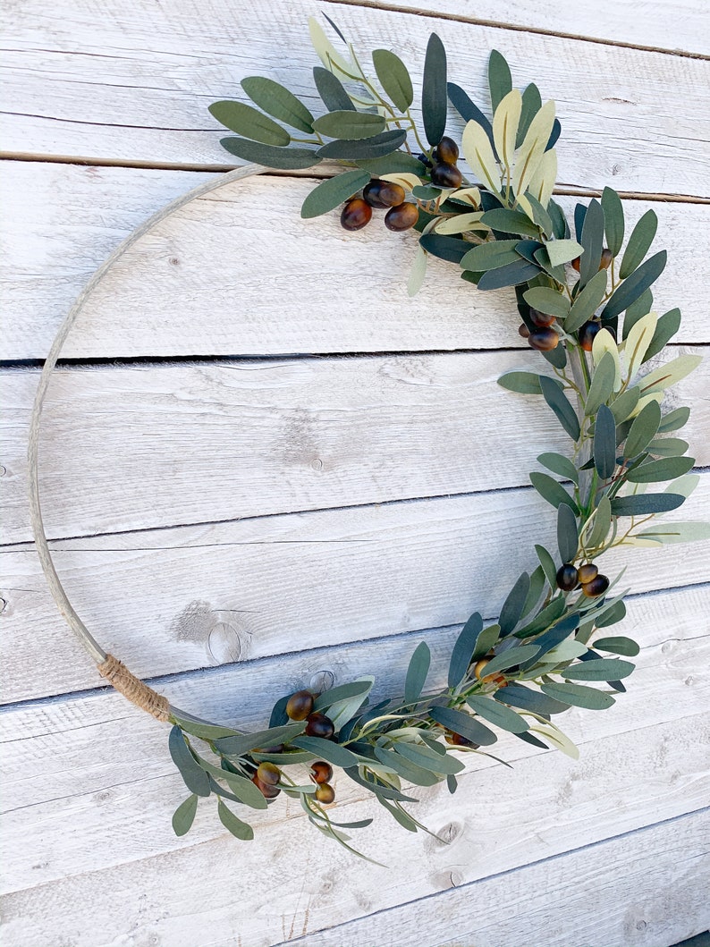 May include: A green olive branch wreath with brown olives, wrapped around a natural wood hoop.