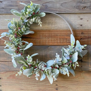 May include: A frosted eucalyptus and berry wreath with red berries on a rustic wood background.