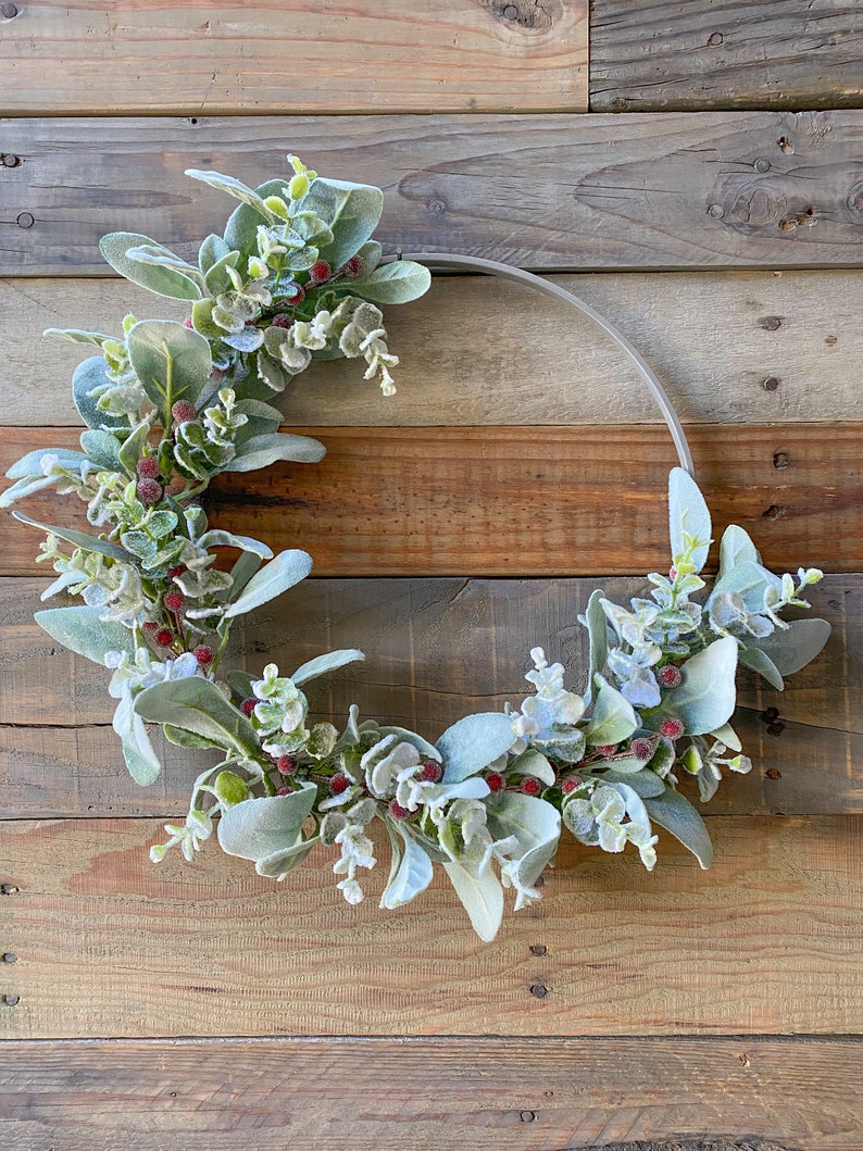May include: A frosted eucalyptus and berry wreath with red berries on a rustic wood background.